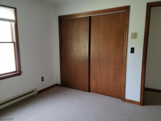 unfurnished bedroom with a baseboard heating unit, a closet, carpet flooring, and baseboards