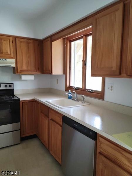 kitchen featuring stainless steel appliances, a sink, brown cabinets, light countertops, and under cabinet range hood