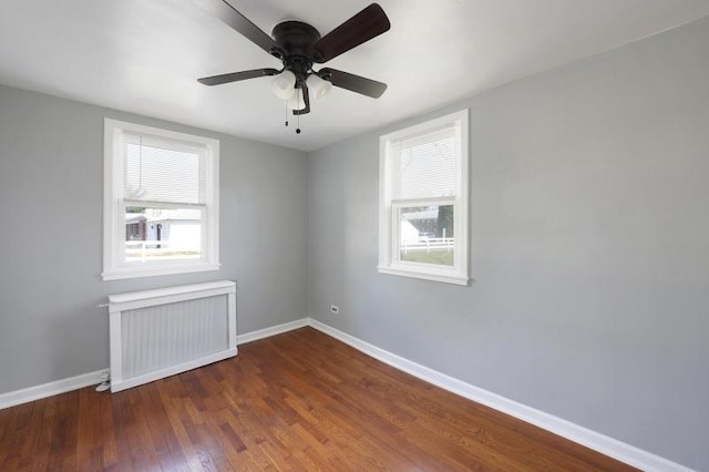 spare room featuring dark wood-style flooring, baseboards, a ceiling fan, and radiator