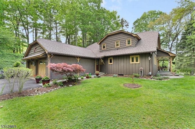 view of front of home with a front yard, board and batten siding, roof with shingles, and driveway
