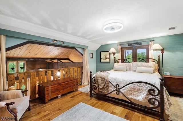bedroom featuring lofted ceiling, wood walls, and wood finished floors
