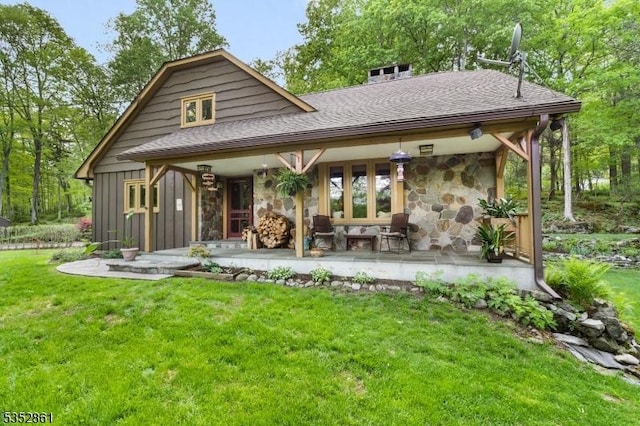 rear view of house featuring stone siding, a yard, a shingled roof, and board and batten siding