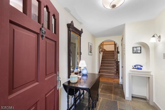 foyer featuring stone tile flooring, arched walkways, stairway, and baseboards