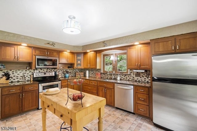 kitchen with appliances with stainless steel finishes, brown cabinetry, a sink, decorative backsplash, and glass insert cabinets