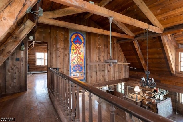 hall with wooden walls, an inviting chandelier, and vaulted ceiling with beams