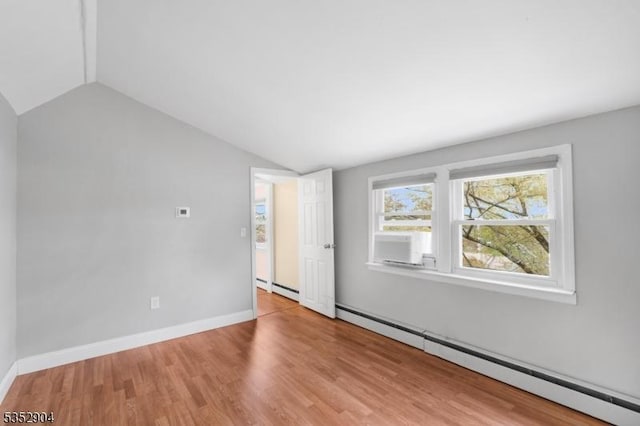 spare room featuring baseboards, baseboard heating, vaulted ceiling, and wood finished floors
