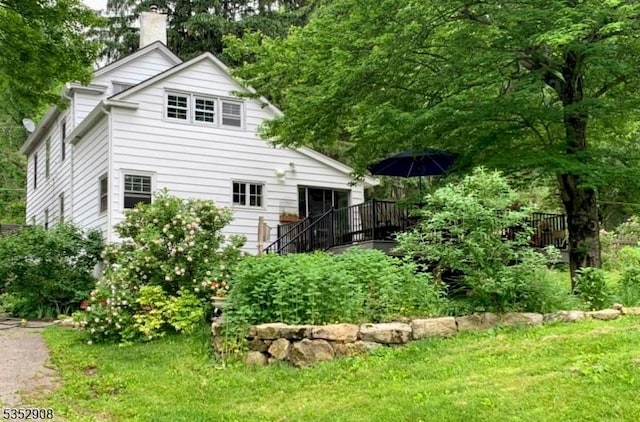 back of property featuring a chimney, a wooden deck, and a yard