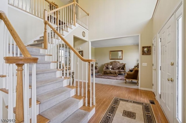 entryway featuring stairway, a towering ceiling, wood finished floors, and visible vents