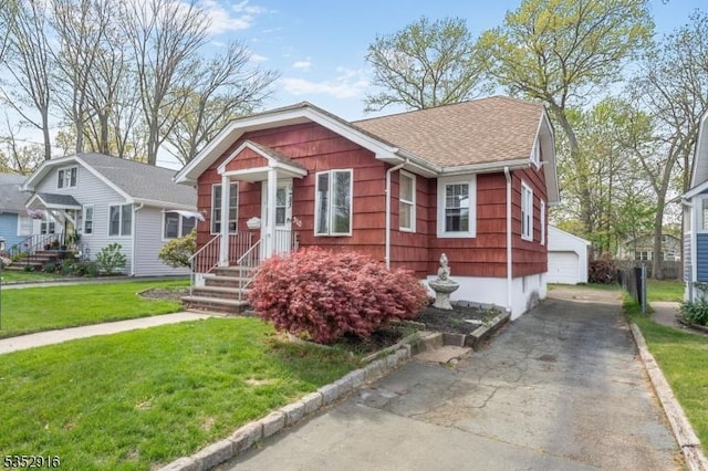 bungalow-style home with a garage, an outbuilding, a front yard, and roof with shingles