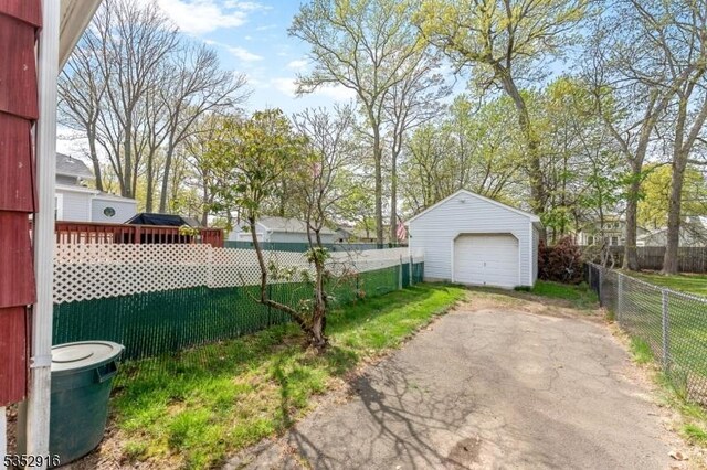 view of yard with an outdoor structure, a detached garage, driveway, and fence