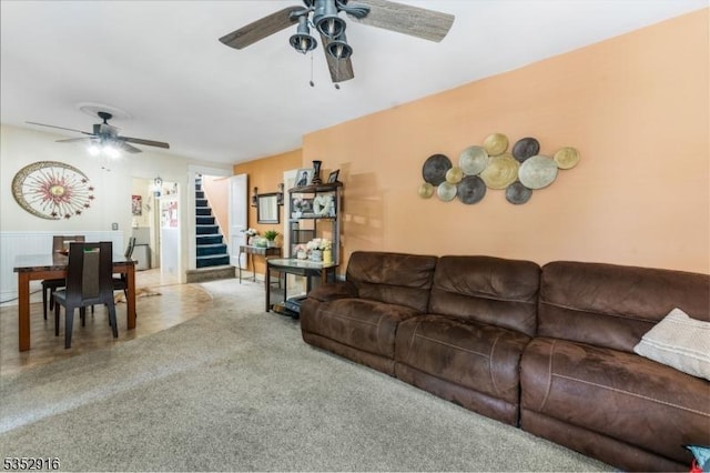 carpeted living area with stairway and ceiling fan