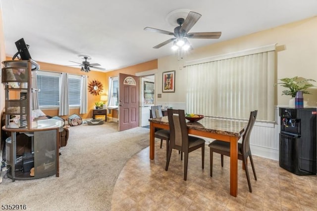 carpeted dining area featuring wainscoting and ceiling fan