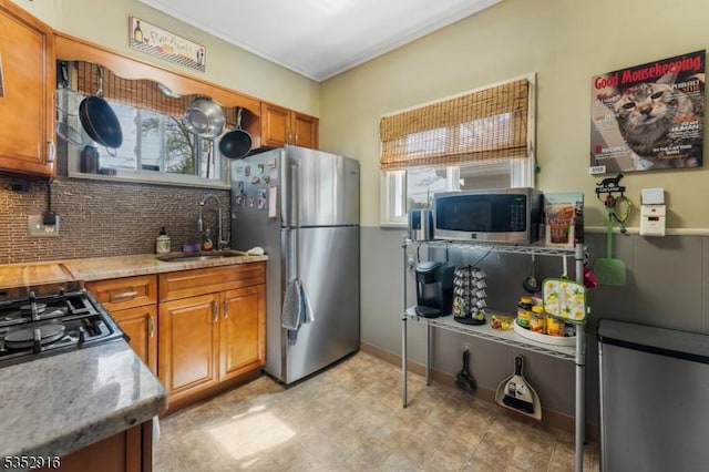 kitchen featuring decorative backsplash, stainless steel appliances, light countertops, brown cabinets, and a sink