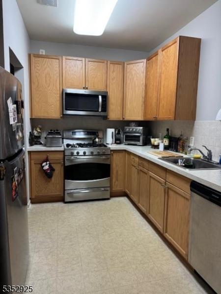 kitchen with light countertops, stainless steel appliances, a sink, and a toaster