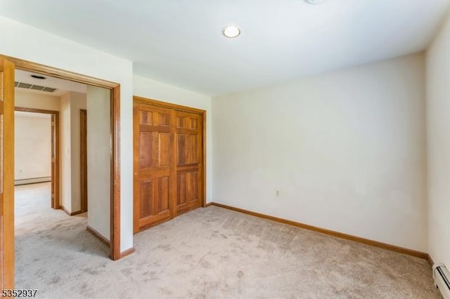 unfurnished bedroom with a baseboard heating unit, a closet, light colored carpet, and baseboards