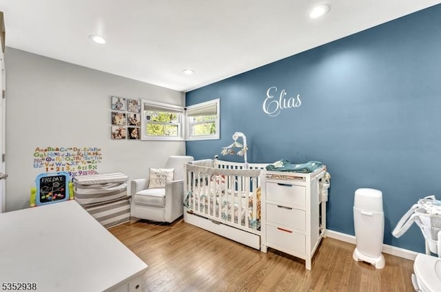 bedroom featuring a nursery area, baseboards, recessed lighting, and wood finished floors