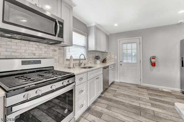 kitchen featuring white cabinets, a sink, light countertops, stainless steel appliances, and light wood-type flooring