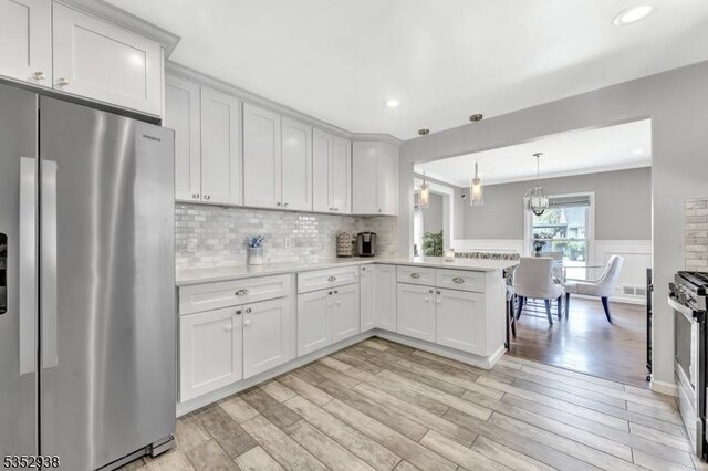 kitchen with white cabinets, appliances with stainless steel finishes, light wood-style floors, light countertops, and a peninsula