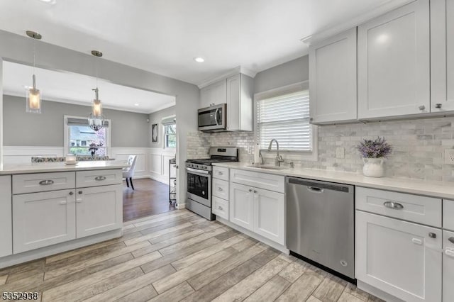 kitchen featuring light countertops, a wainscoted wall, a sink, light wood finished floors, and appliances with stainless steel finishes