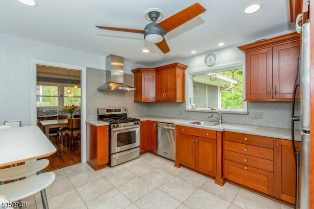 kitchen featuring wall chimney range hood, ceiling fan, appliances with stainless steel finishes, a sink, and light countertops