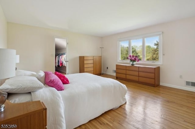 bedroom featuring light wood finished floors, a closet, visible vents, baseboards, and a spacious closet