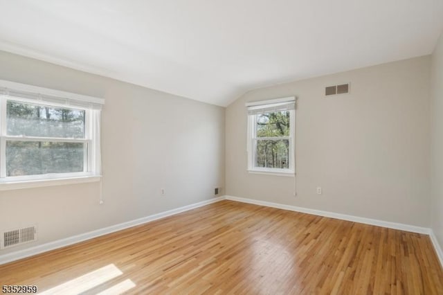 unfurnished room with visible vents, light wood finished floors, vaulted ceiling, and baseboards