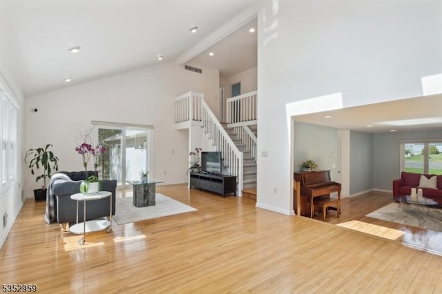 living room featuring stairway, beam ceiling, light wood-style floors, high vaulted ceiling, and visible vents