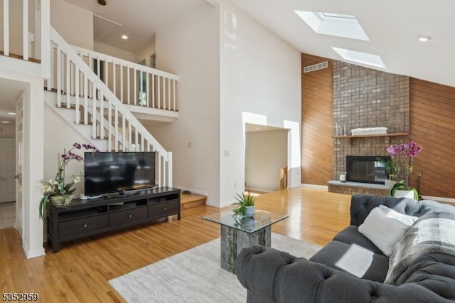 living area with visible vents, a fireplace, wood finished floors, high vaulted ceiling, and a skylight