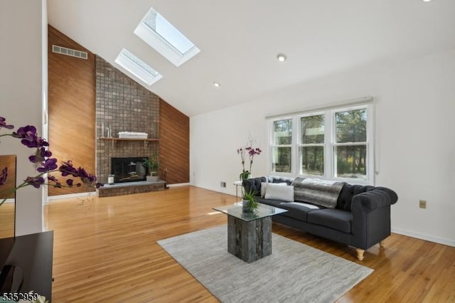 living room with a fireplace, high vaulted ceiling, light wood-type flooring, visible vents, and a skylight