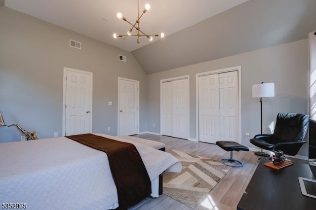 bedroom with visible vents, a chandelier, light wood finished floors, vaulted ceiling, and two closets