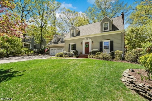 new england style home with an attached garage, driveway, a shingled roof, and a front yard