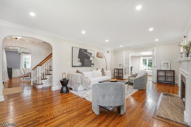 living room featuring ornamental molding, a fireplace with flush hearth, wood finished floors, stairway, and arched walkways
