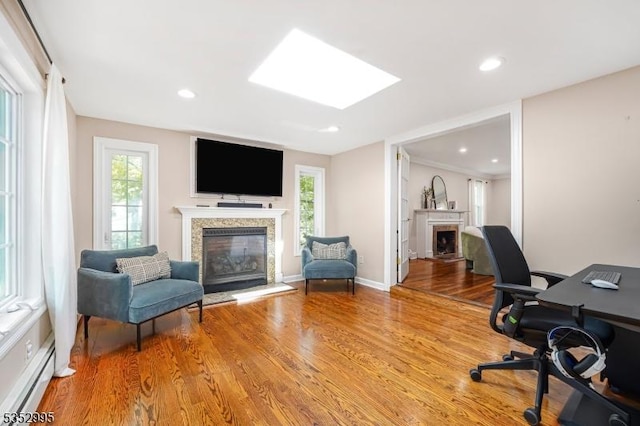 office space featuring a fireplace with raised hearth, a baseboard heating unit, light wood-style flooring, and recessed lighting