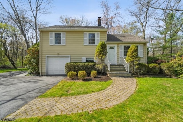 tri-level home featuring a garage, a chimney, a front yard, and aphalt driveway