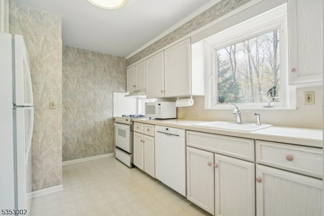 kitchen with a sink, light countertops, baseboards, light floors, and white appliances