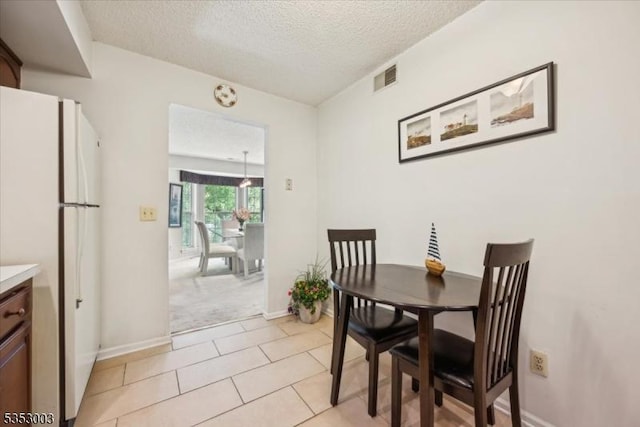 dining room with a textured ceiling, light carpet, baseboards, and light tile patterned floors