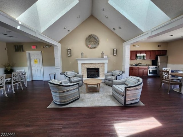 living area with high vaulted ceiling, a skylight, dark wood-style floors, and a glass covered fireplace