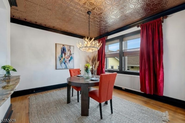 dining space with wood finished floors, a chandelier, radiator heating unit, an ornate ceiling, and baseboards