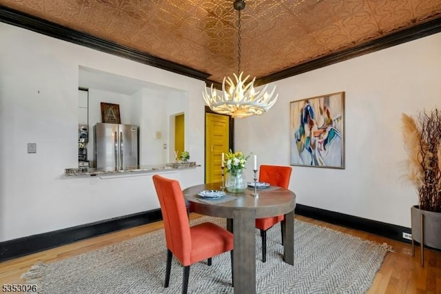dining space with wood finished floors, ornamental molding, an ornate ceiling, baseboards, and a notable chandelier
