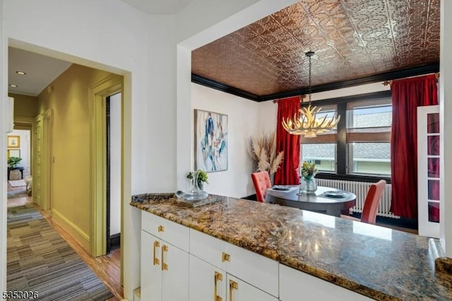 kitchen with an inviting chandelier, dark stone countertops, an ornate ceiling, white cabinetry, and pendant lighting