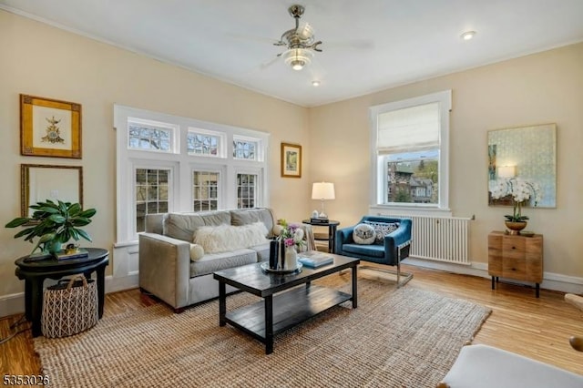 living area with baseboards, a ceiling fan, and light wood-style flooring