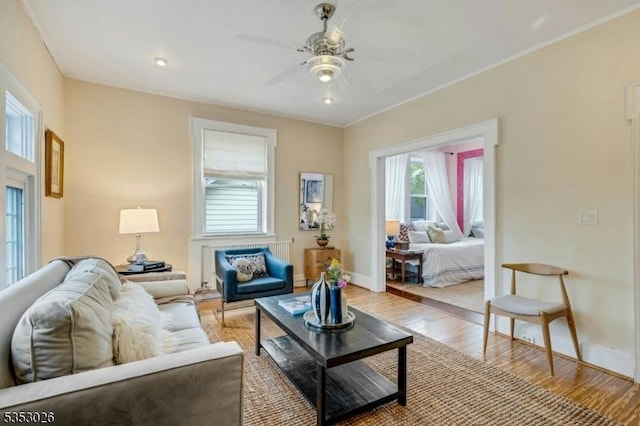 living room featuring baseboards, ornamental molding, ceiling fan, and light wood finished floors
