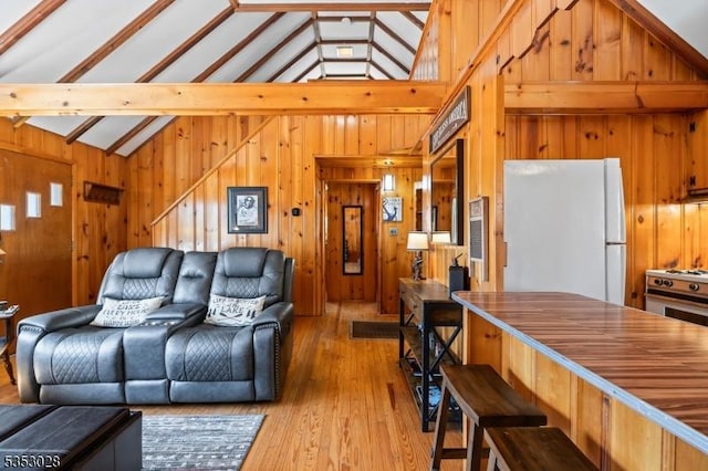 living room featuring wood walls, vaulted ceiling with beams, and light wood finished floors