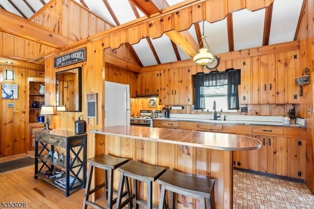 kitchen featuring range with gas stovetop, a kitchen breakfast bar, wooden walls, a peninsula, and freestanding refrigerator