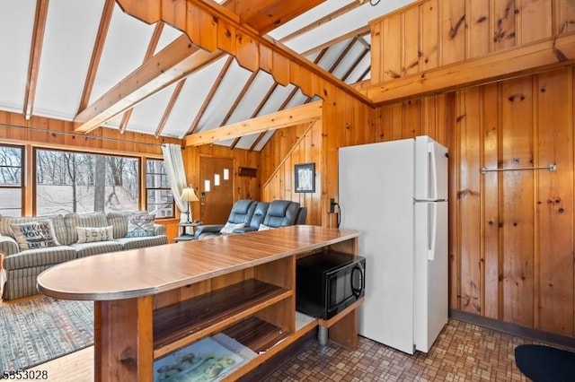 kitchen featuring black microwave, wooden walls, open floor plan, and freestanding refrigerator