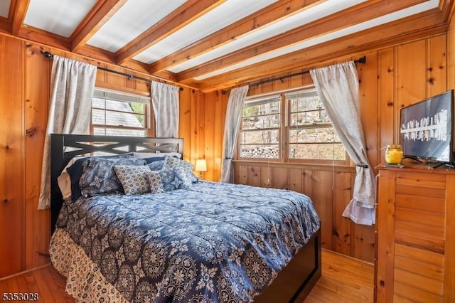 bedroom with beam ceiling, wooden walls, and wood finished floors