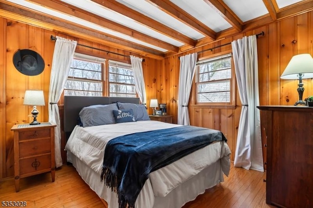 bedroom featuring beamed ceiling, wood walls, and light wood-style floors
