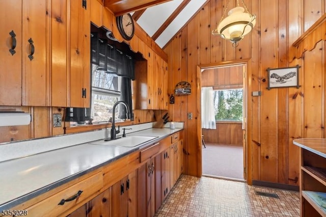 kitchen with a sink, wood walls, light countertops, vaulted ceiling with beams, and brown cabinetry