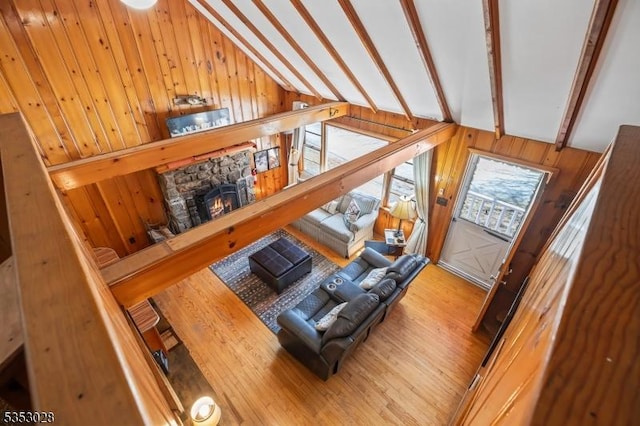 living area featuring vaulted ceiling with beams, wooden walls, wood finished floors, and a fireplace