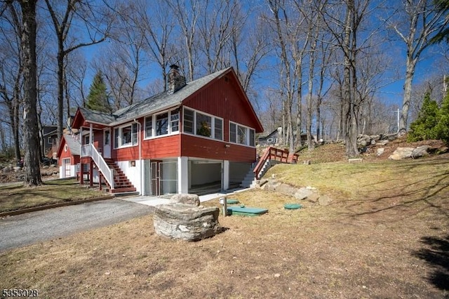 view of property exterior featuring a sunroom, stairway, aphalt driveway, and a chimney